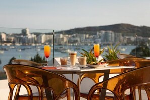 A table with breakfast items and drinks, overlooking a marina and cityscape. - Hotel THB Naeco Ibiza - Adults Only (Sant Josep de sa Talaia)