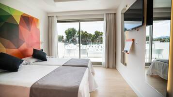 Een hotelkamer met twee bedden, een groot raam met uitzicht op de omgeving en een flatscreen televisie aan de wand.