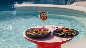 A table with two plates of food and a glass of drink by a pool.