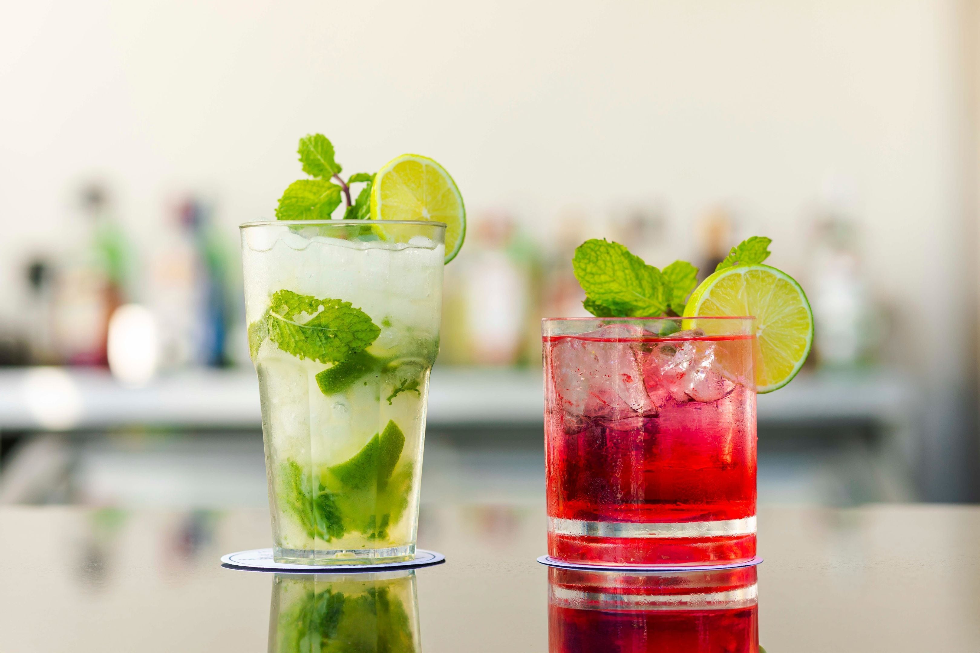 Dos vasos de bebidas heladas con rodajas de lima y hojas de menta, sobre una superficie reflectante.