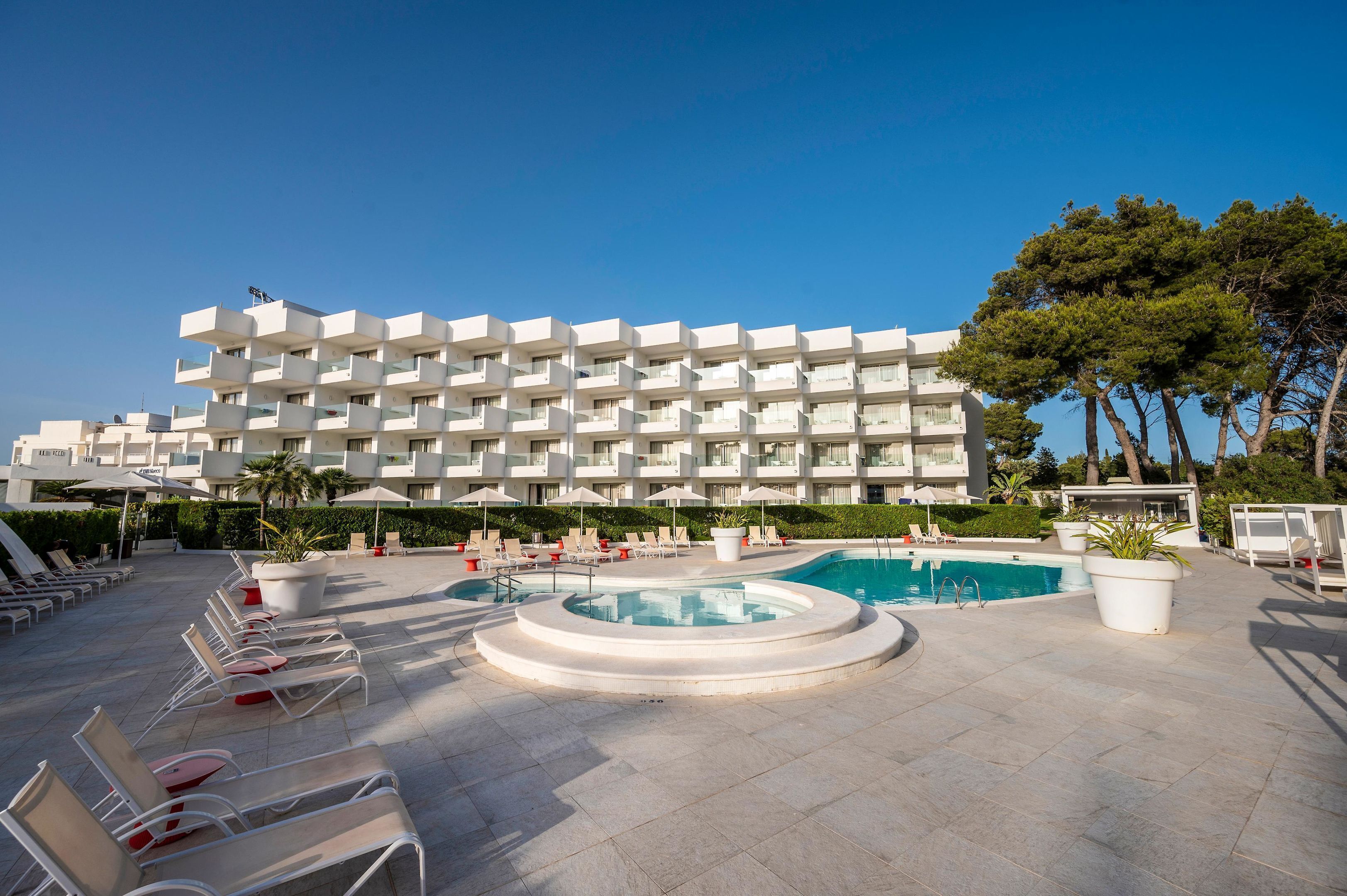 Un hôtel doté d’une piscine, de chaises longues et d’un grand bâtiment avec des balcons.