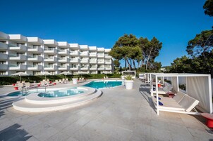 Un área de piscina con sillones de descanso, una piscina circular y un edificio con balcones al fondo.