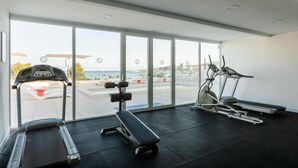 Un gimnasio con cintas de correr, una bicicleta estática y una banca. Amplias ventanas ofrecen vistas al exterior.