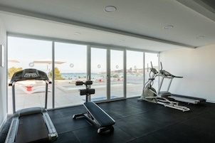 Un gimnasio con cintas de correr, una bicicleta estática y una banca. Amplias ventanas ofrecen vistas al exterior.