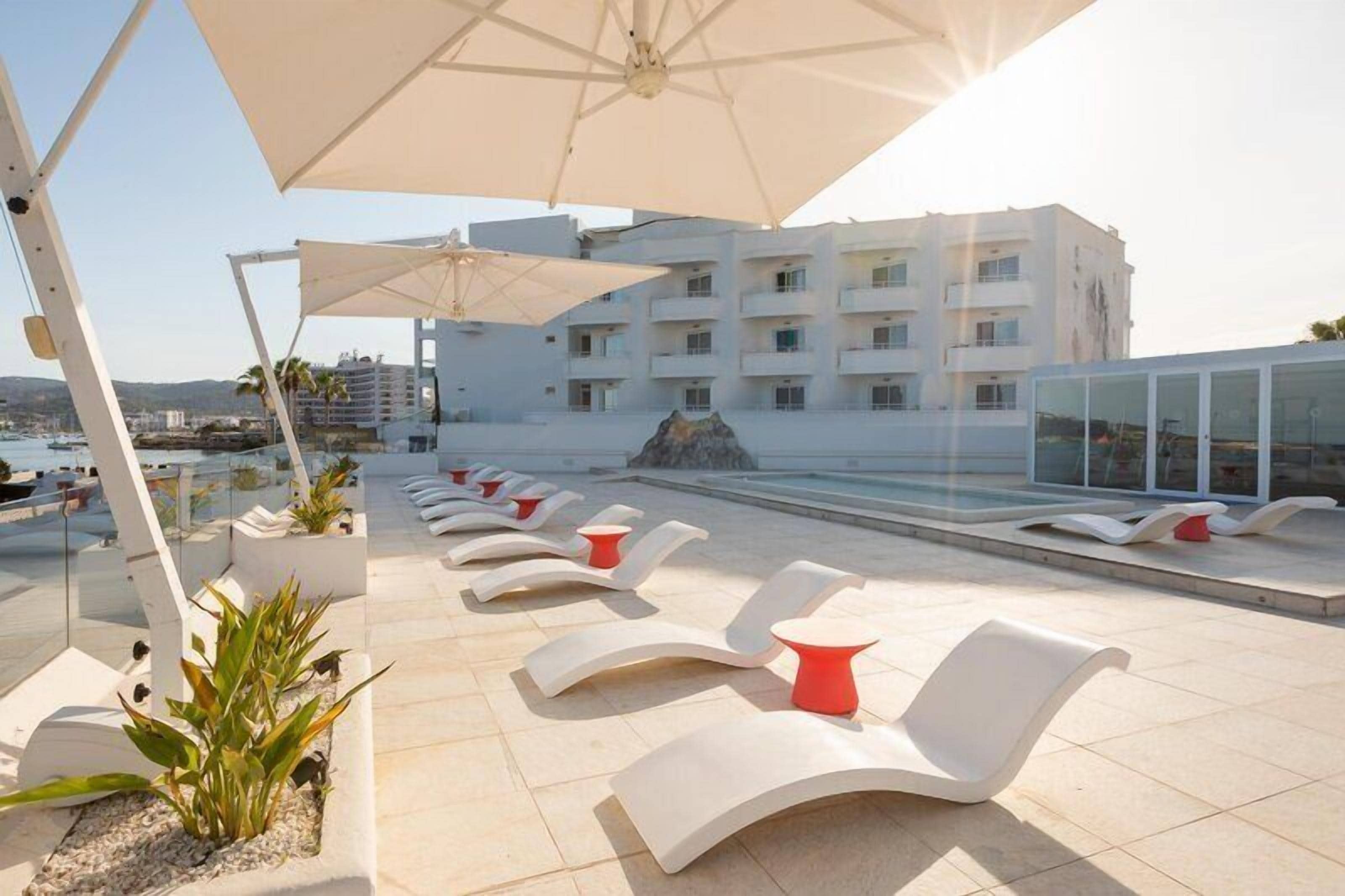 A rooftop terrace with sun loungers, umbrellas, and a pool view.