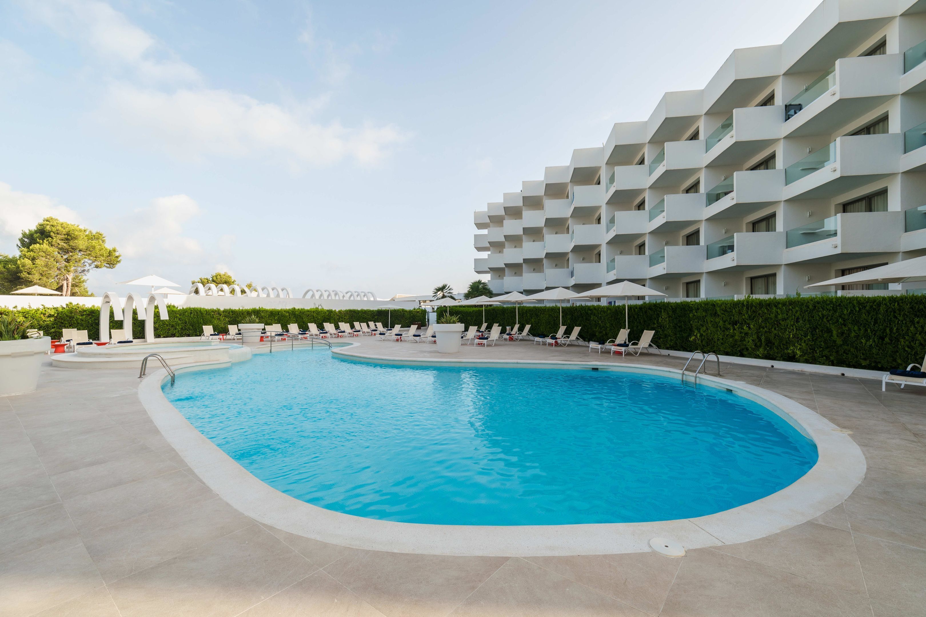 A swimming pool with lounge chairs and umbrellas, surrounded by a modern building with balconies.