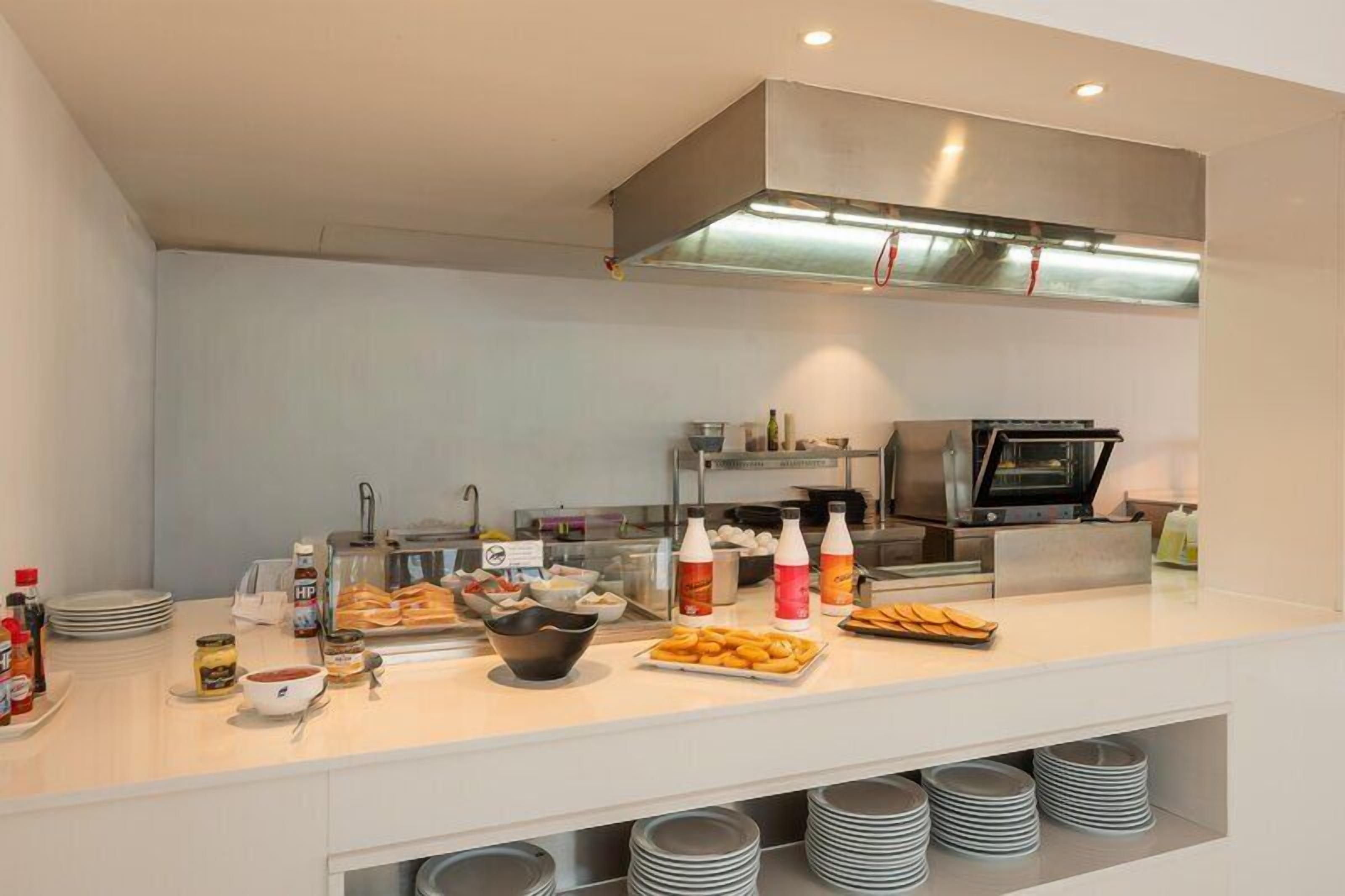 A modern kitchen with a stainless steel range hood, a microwave, and a buffet setup with various food items and condiments.