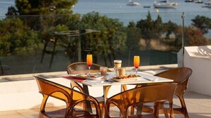 Una mesa con alimentos para el desayuno, sillas transparentes y vista al mar y embarcaciones.