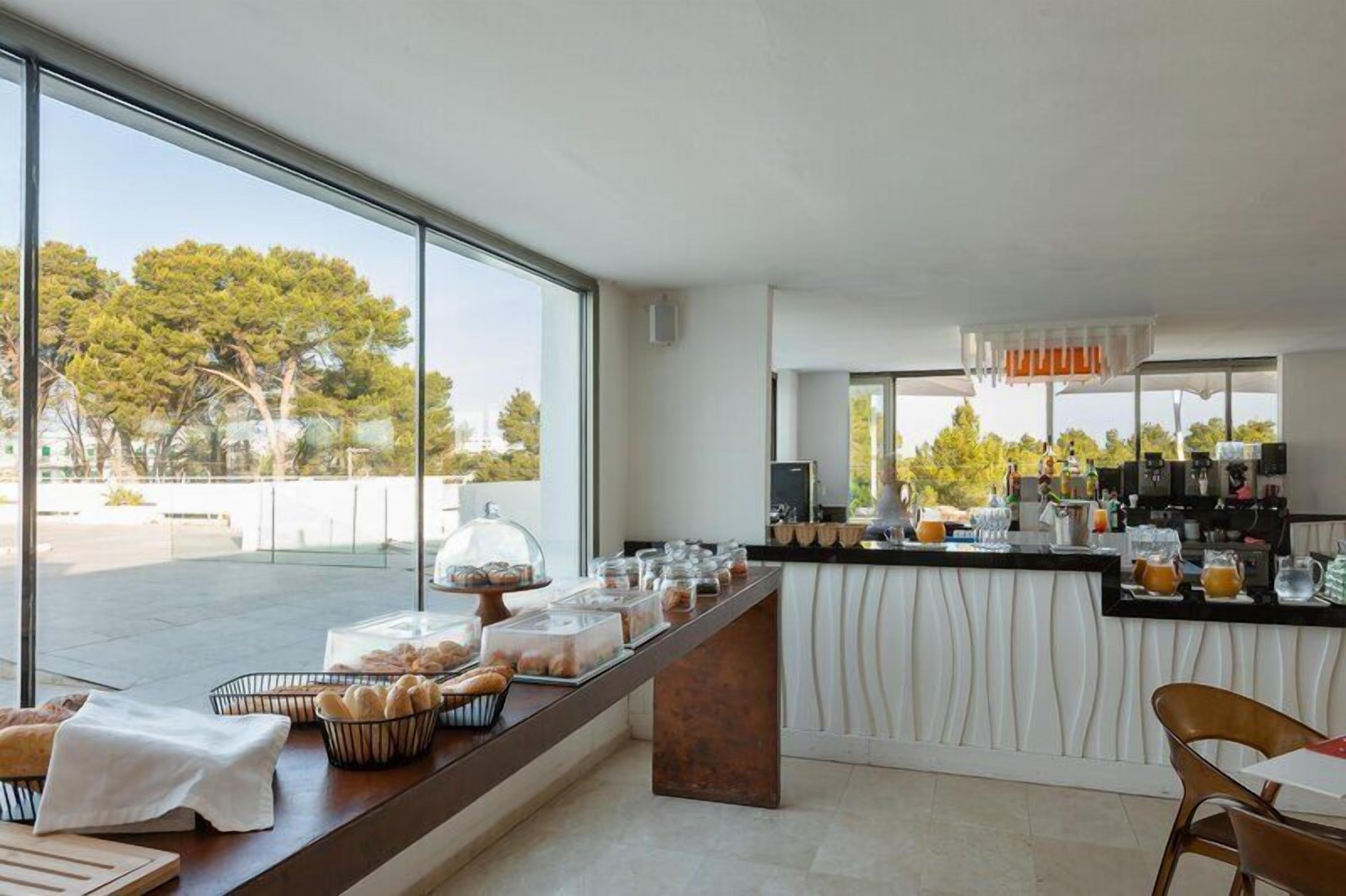 A breakfast bar with pastries, a coffee station, and a view of trees through large windows.