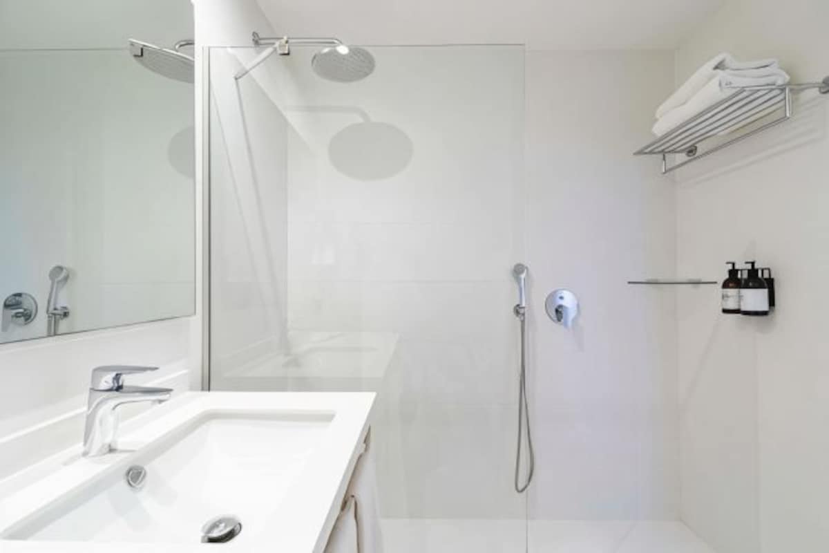 A modern bathroom with a glass shower enclosure, a white sink, and a towel rack.