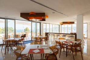 A spacious dining area with tables and chairs, large windows with a view, and modern orange pendant lighting. - Hotel THB Naeco Ibiza - Adults Only (Sant Josep de sa Talaia)