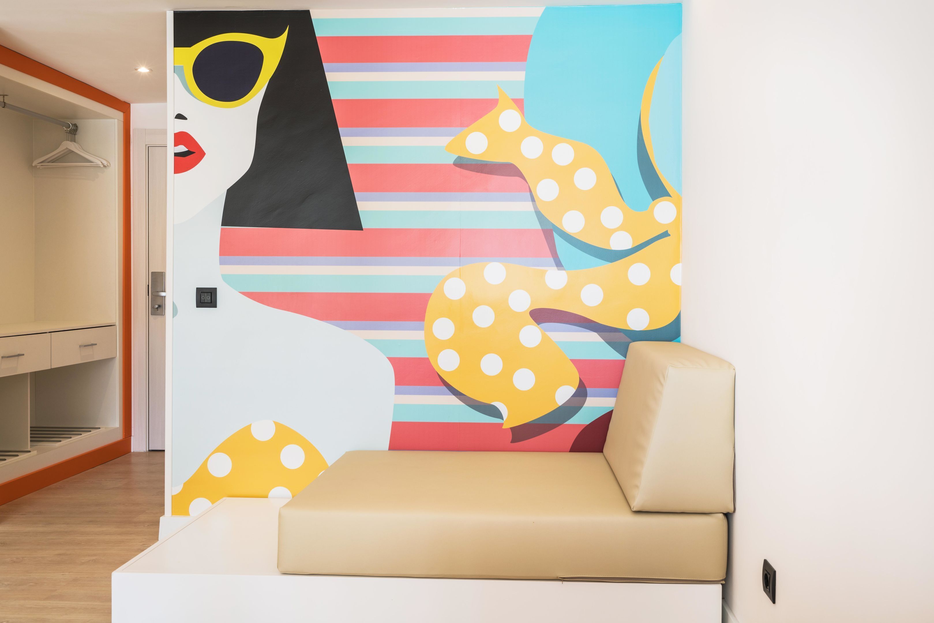 A modern room with a sofa, a colorful abstract mural, and a wooden floor.