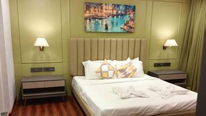 Quarto de hotel com cama, duas mesas de cabeceira, um quadro e um ventilador de teto.