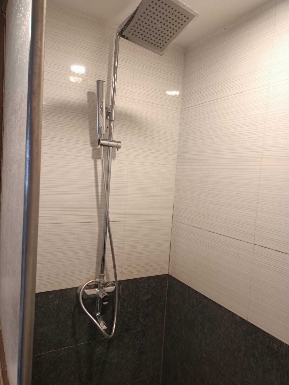 Eine Dusche mit Handbrause und Deckenbrause in einer Raumecke, Wände und Boden sind mit Fliesen belegt.