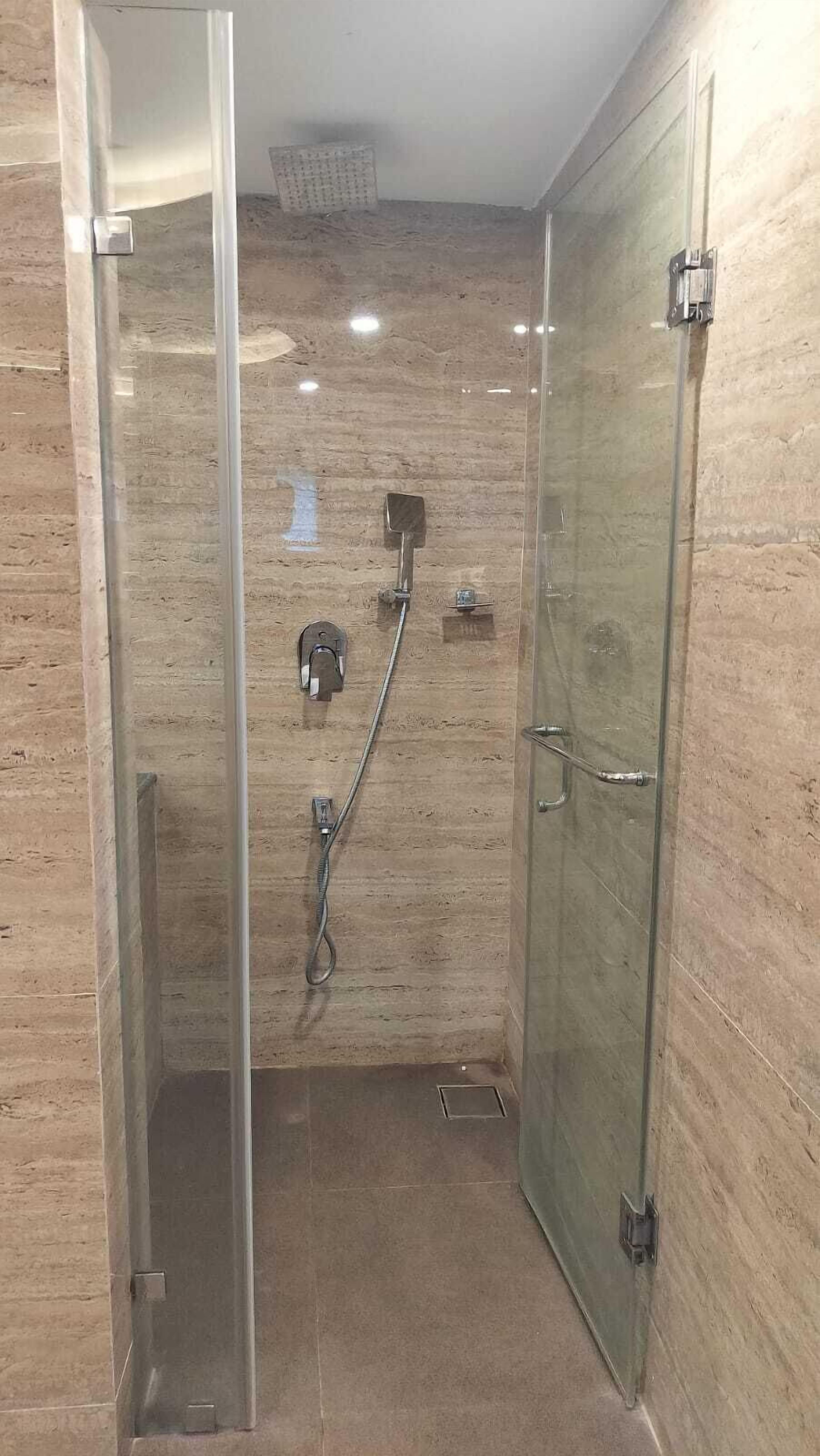 A glass-enclosed shower stall with a handheld showerhead, a wall-mounted control panel, and a glass door.