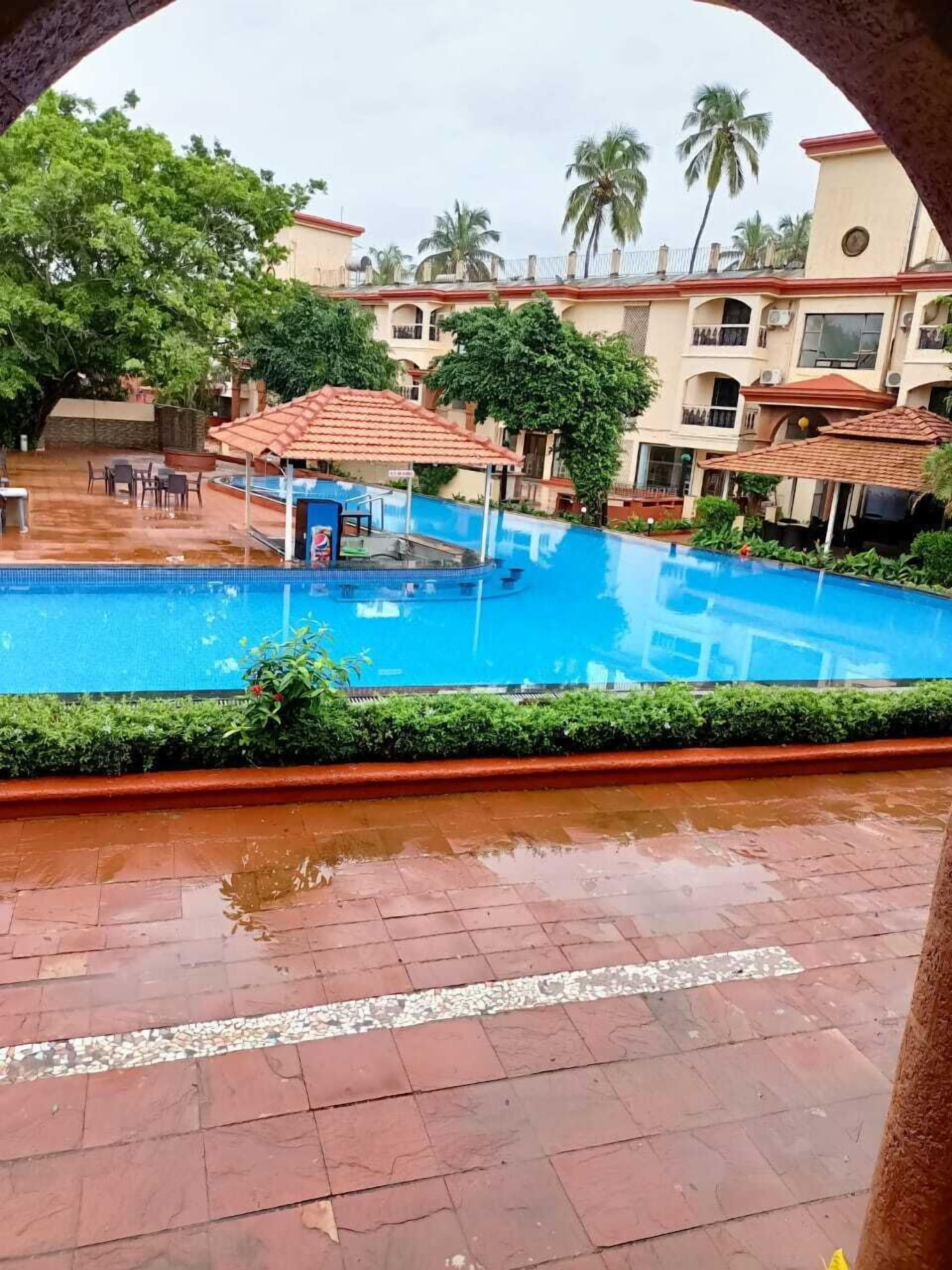 Una piscina con sombrillas, rodeada de vegetación y edificios.