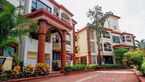 Um hotel com vários andares, varandas, pilares vermelhos e um caminho de pedras.