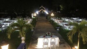 A formal outdoor dining area with tables and chairs arranged in rows, flanked by palm trees and illuminated by overhead lights. - Hacienda San Pedro Nohpat (Kanasín)