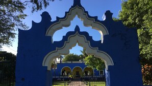 A blue gate with white trim and a decorative archway, leading to a building with a balcony. - Hacienda San Pedro Nohpat (Kanasín)