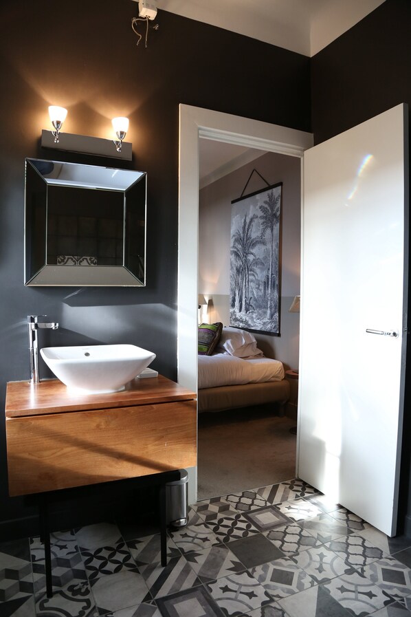 A modern bathroom with a large mirror, a white sink, and a wooden vanity.