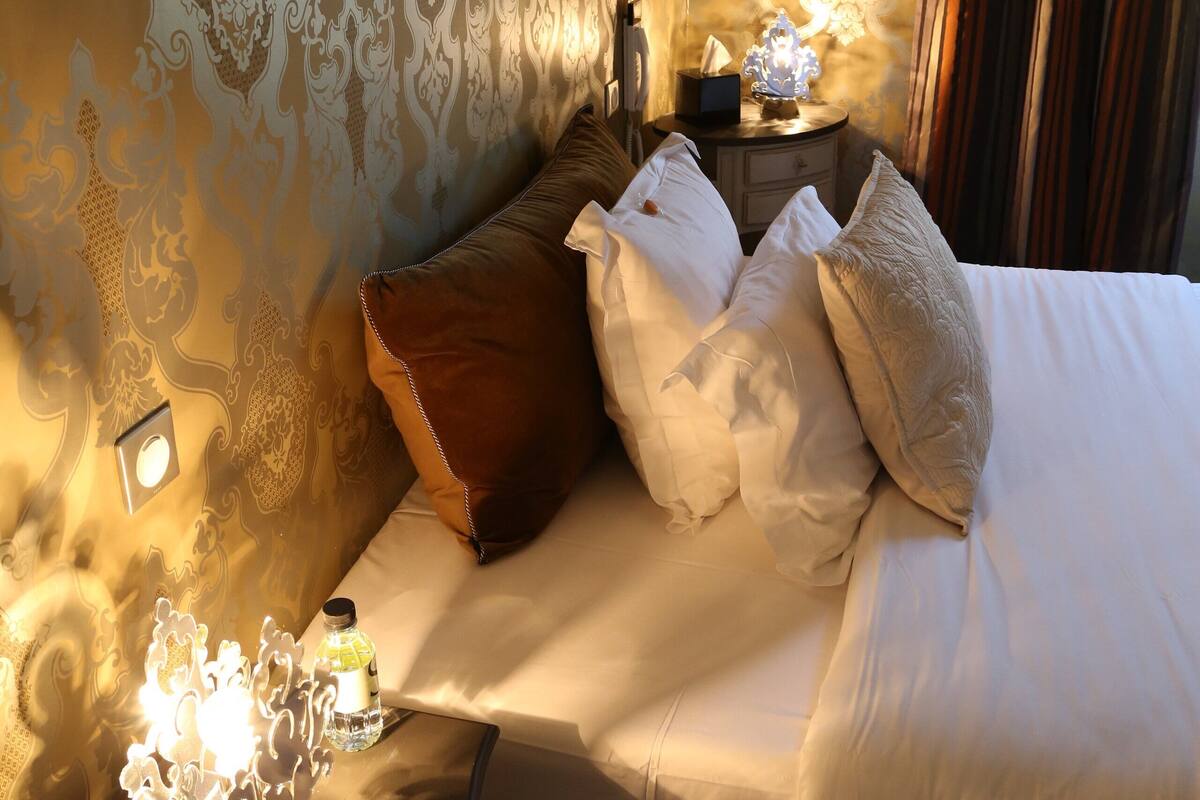 A hotel room with a bed, pillows, a nightstand, and a wall with a patterned design.