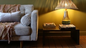 Ein gemütliches Wohnzimmer mit einer Couch, einem Teppich mit Muster, einer Lampe und einem Bücherregal mit Büchern und Dekoration.