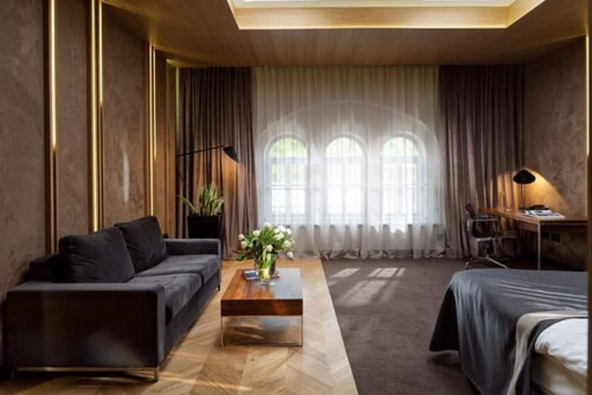 Une chambre moderne avec un canapé, une table basse en bois, un bureau et un lit. On y trouve des rideaux, une plante et une lampe.