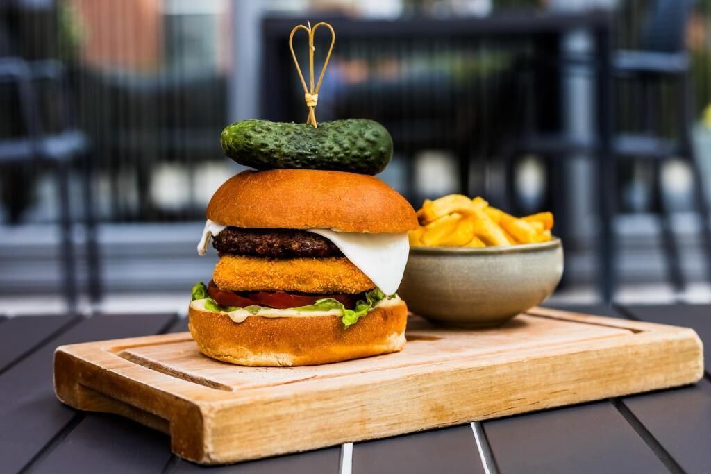 A burger with a pickle on top, served with fries on a wooden board.
