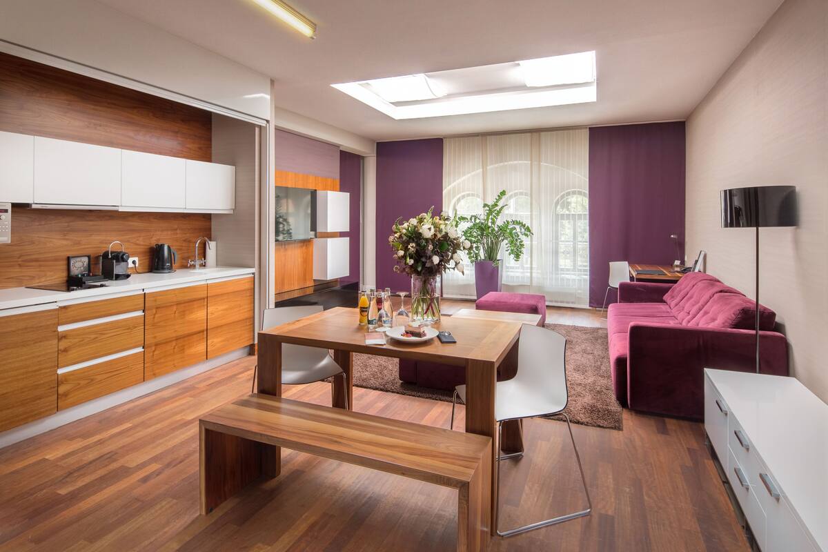 Un salon moderne avec une table à manger en bois, un canapé et un coin cuisine doté de meubles en bois et d’un four encastré.
