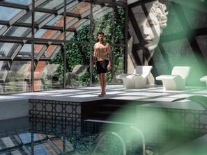 Ein moderner Innenpoolbereich mit Glasdach, einer Statue und Liegestühlen.