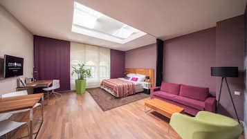 Moderni hotellihuone, jossa on sänky, sohva, työpöytä ja televisio.