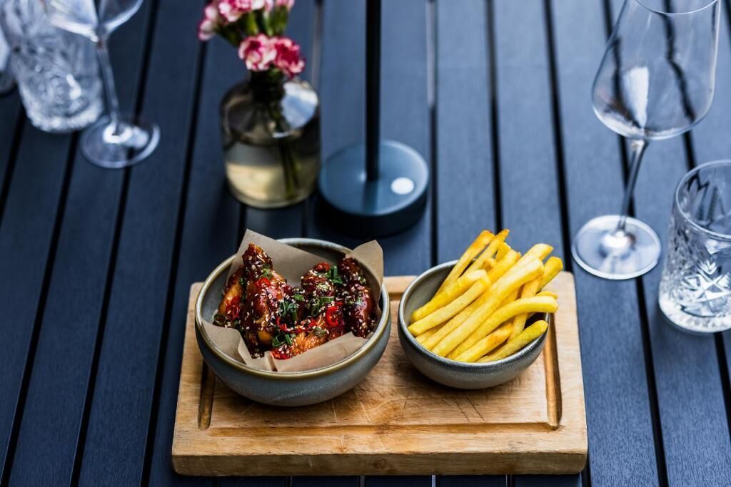 A wooden table with a bowl of fried chicken and a bowl of French fries.