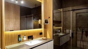 Un baño moderno con un espejo grande, paneles de madera, un lavabo y cabina de ducha con mampara de vidrio.
