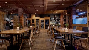 Un restaurant avec des tables et des chaises en bois, des murs en briques et un plafond avec des lambris en bois.