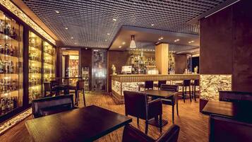 Un área de bar con suelo de madera, taburetes y estantes llenos de botellas.