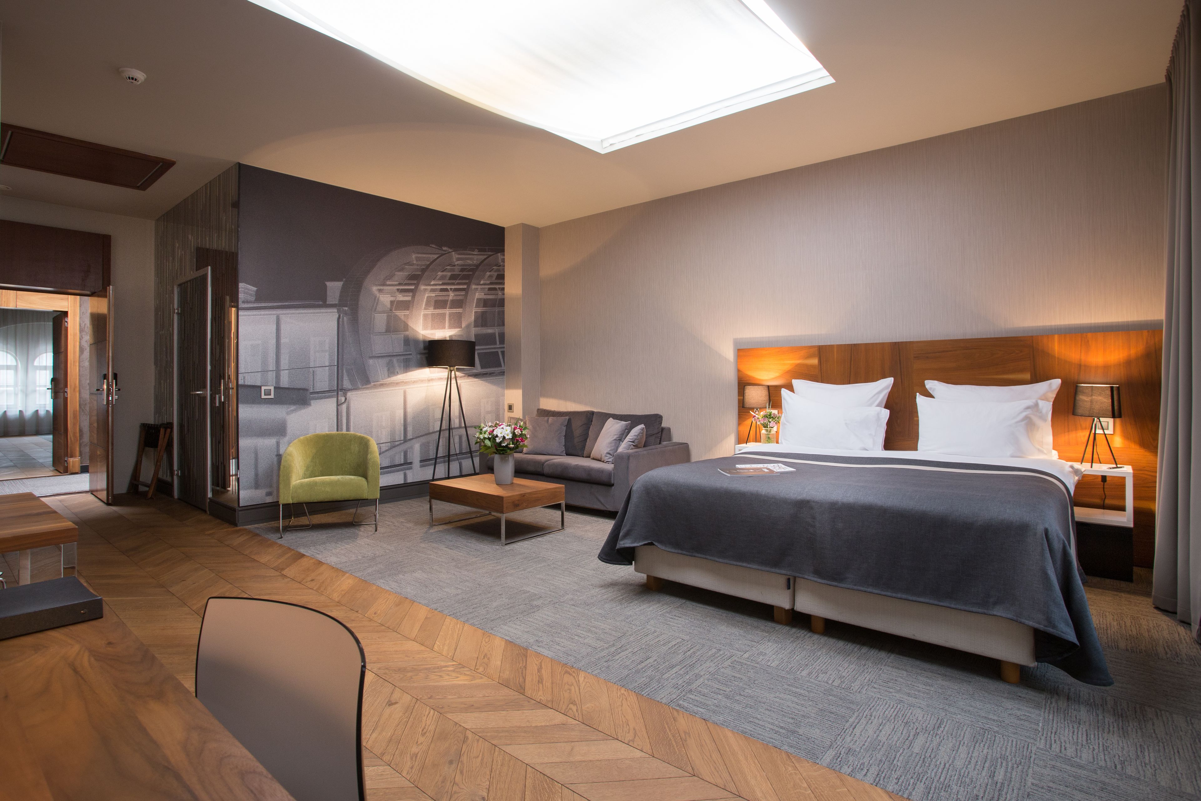 A modern hotel room with a large bed, a sofa, a desk, and a chair.