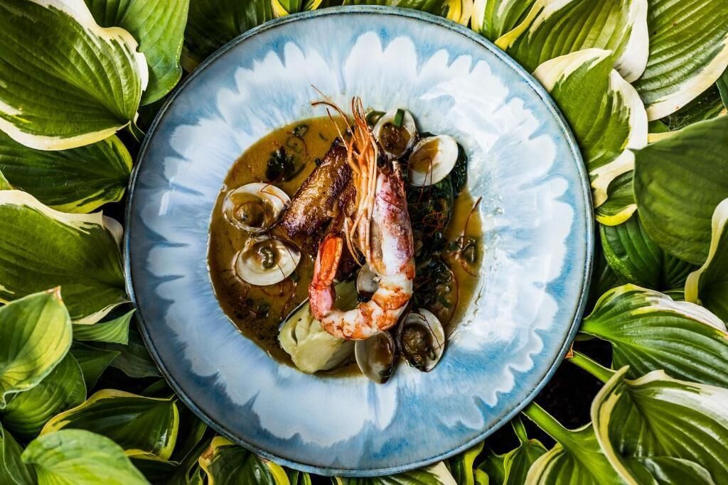 A seafood dish on a blue plate surrounded by green leaves.