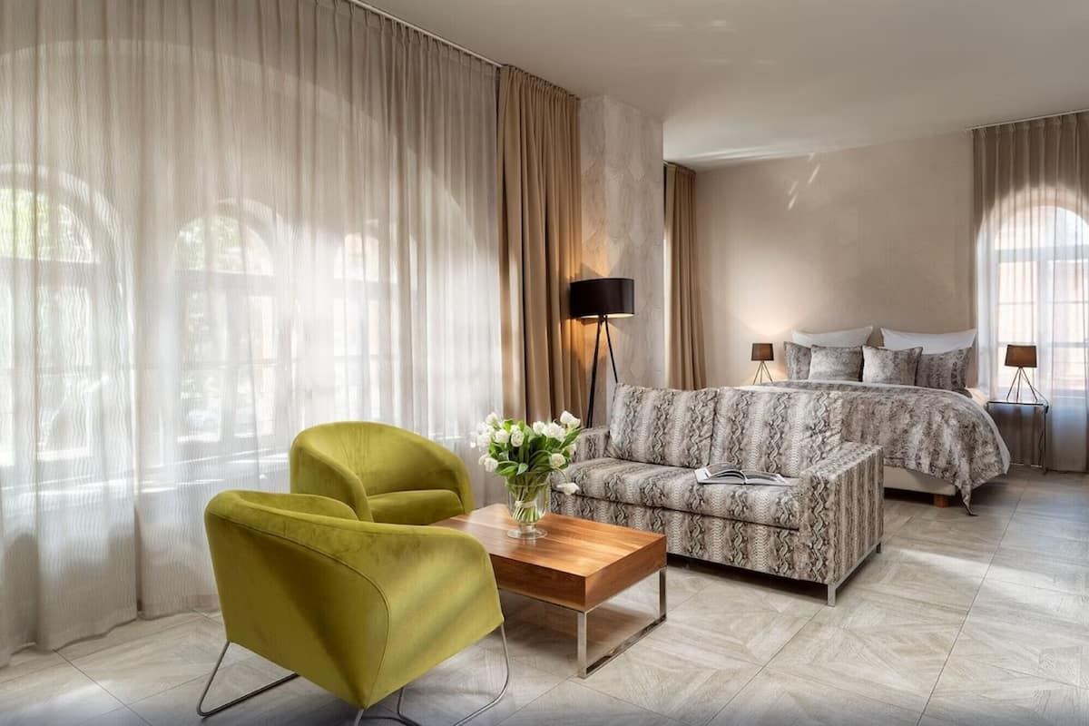 Une chambre d’hôtel moderne avec un grand lit, un canapé, un fauteuil vert et une table basse en bois.