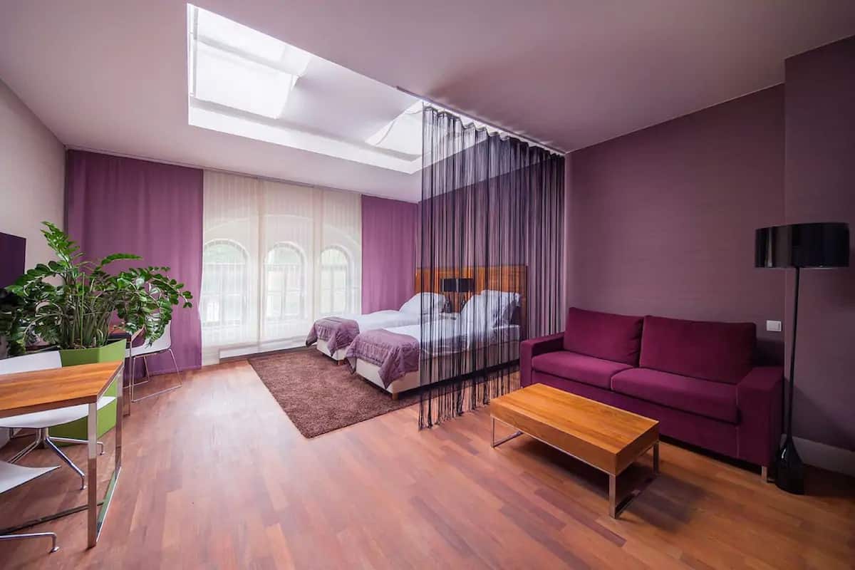 Une chambre à coucher moderne avec un lit, un canapé violet, une table basse en bois et une plante en pot.