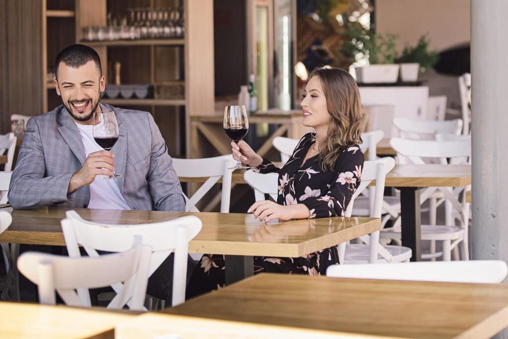 A man and a woman sitting at a table in a restaurant, both holding wine glasses.