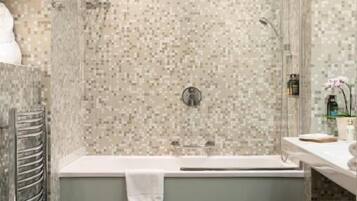 A modern bathroom with a mosaic tile shower wall, a freestanding bathtub, and a toilet.