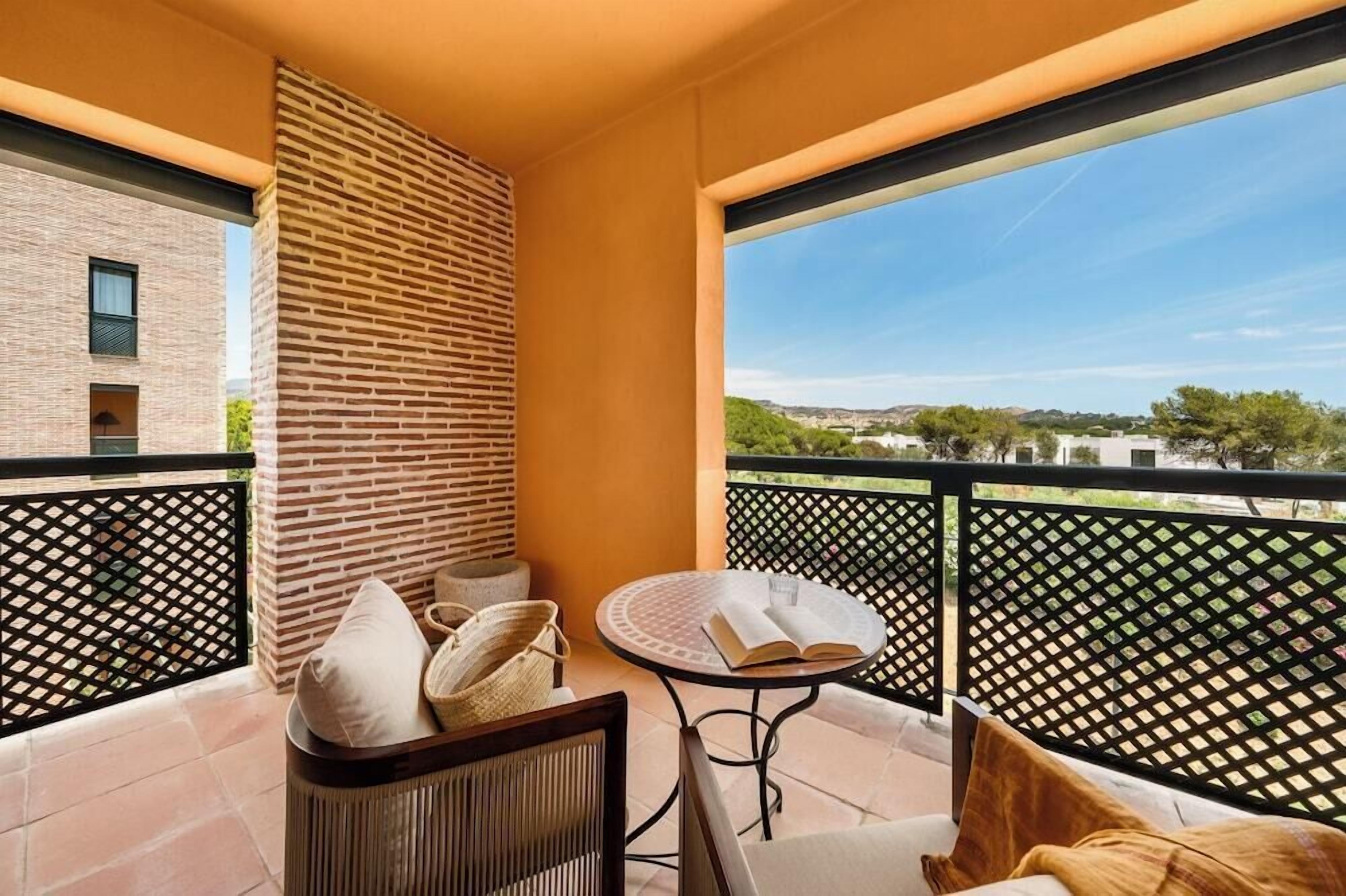 A balcony with a view of a cityscape, a brick wall, and a round table with a book.