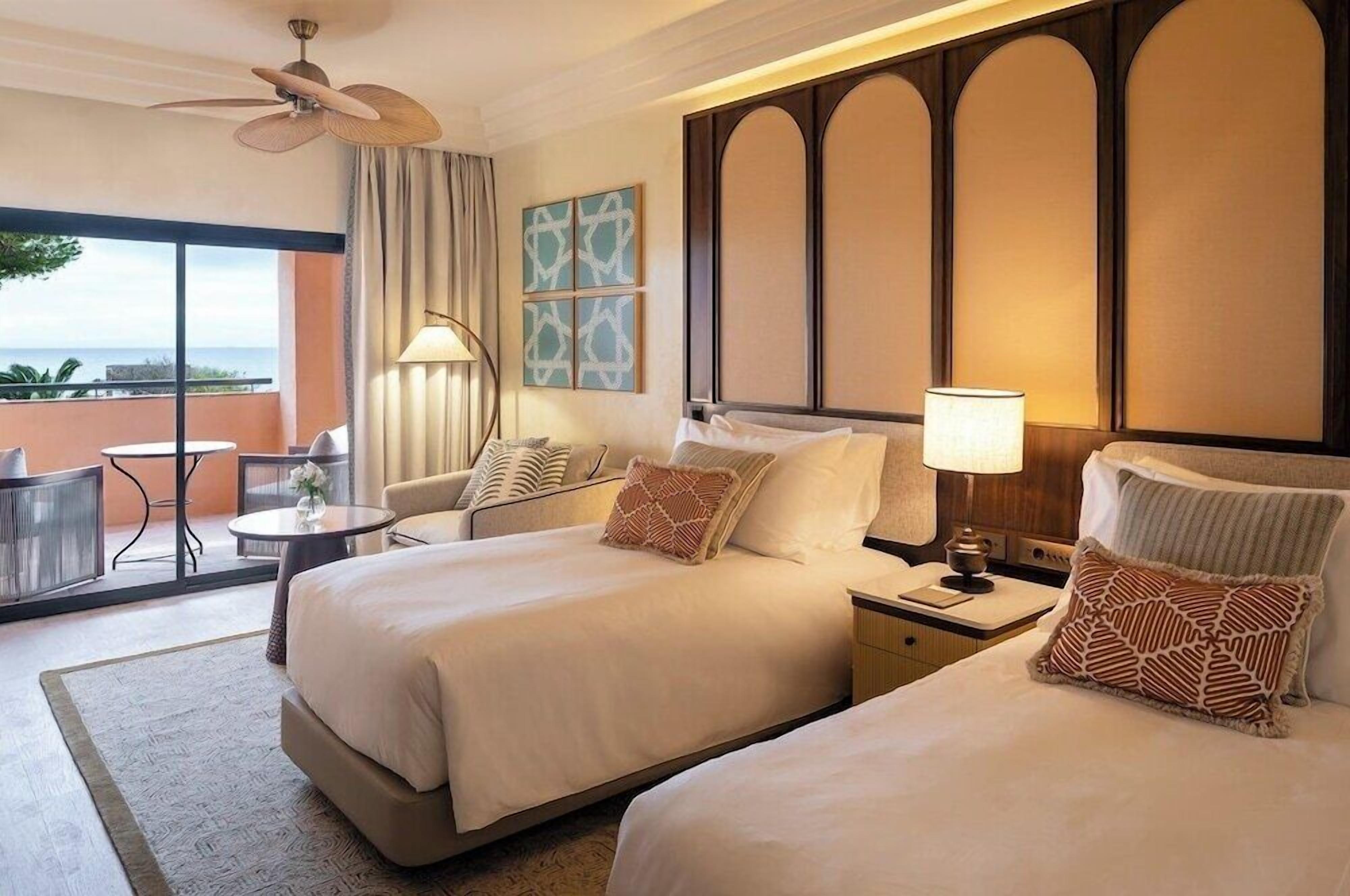 Habitación de hotel con dos camas, balcón, una mesa y vista al océano.