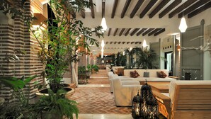 A cozy indoor area with brick walls, potted plants, and a seating area with white sofas and a wooden table.