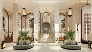 A spacious lobby with a grand staircase, two round seating areas with plants, and a wall of decorative vases.