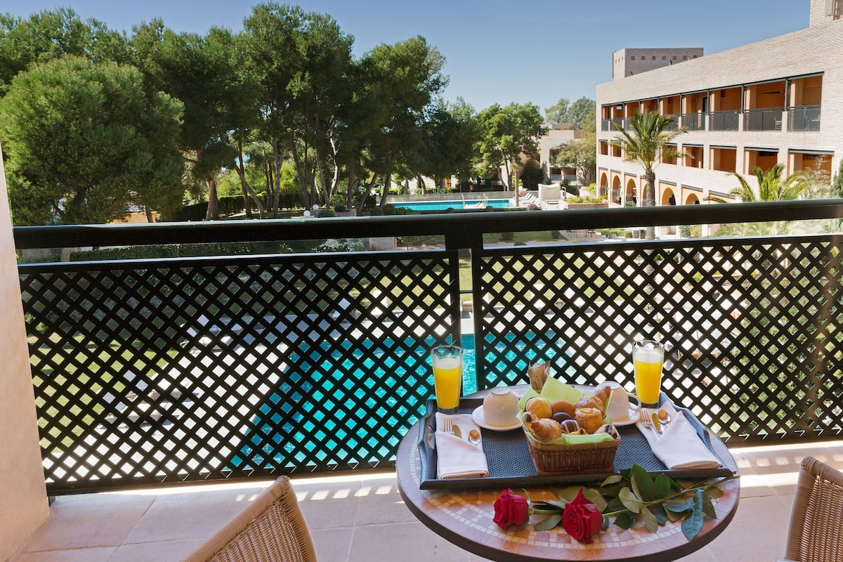 Ein Balkon mit Frühstückstisch, mit Blick auf einen Pool und Bäume.