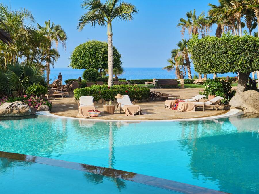 Zona de piscina con sillones de descanso y vista al mar.
