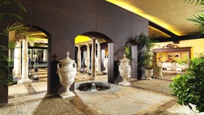 Un hall d’entrée spacieux agrémenté d’une fontaine, de colonnes et de plantes en pot.