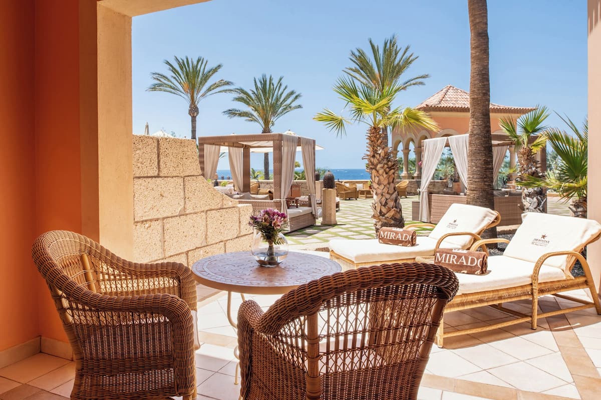Une terrasse meublée de mobilier en osier, avec vue sur la mer et bordée de palmiers.