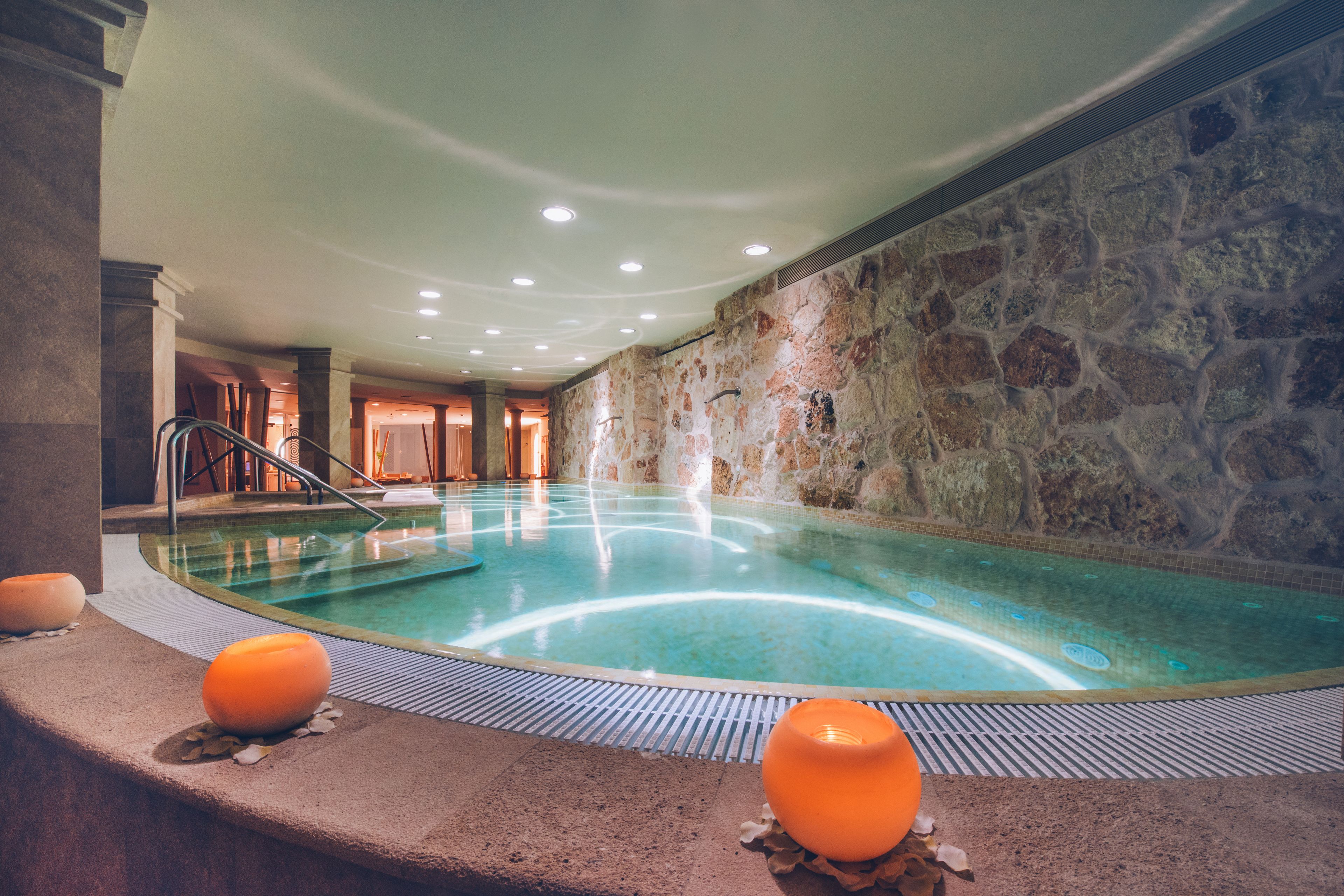 Una piscina interior con paredes de piedra, suelo de baldosas e iluminación empotrada en el techo.